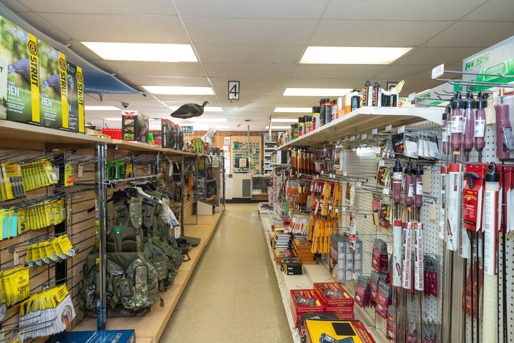 A store aisle lined with products in bright yellow and red packaging including hen decoys and other hunting accessories and camo backpacks